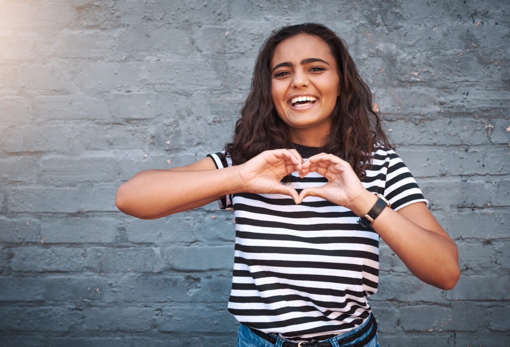 Young woman forming a heart shape with her hands, symbolizing the personal motivation behind her orthodontic journey